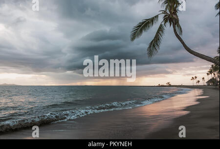 Sunset of tropical beach with palm trees and storm clouds behind in Fiji Stock Photo