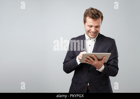 Examining new gadget. Confident young handsome man in blue suit working on digital tablet Stock Photo