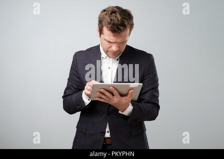 Examining new gadget. Confident young handsome man in shirt and tie working on digital tablet Stock Photo