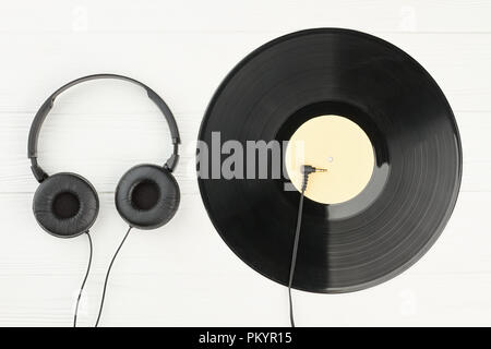 Vinyl record and headphones on white background. Vinyl LP record, audio plug with cable from earphones and headphones. Stock Photo