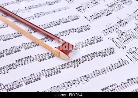 Brown violin bow on musical notes sheets. Stock Photo