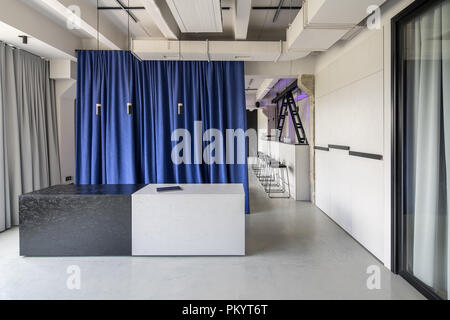 Coworking in a loft style with gray walls and concrete columns. There is a textured black-white reception desk with a laptop, multicolor curtains, bar Stock Photo