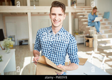 Smiling young casual man with notepad making working notes while working in studio on sunny day Stock Photo