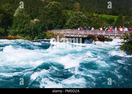 Norway, Olden - August 1, 2018: People at the bridge and turquoise water river from glacier in norwegian mountains Stock Photo