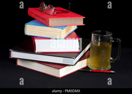 Stacked books with eyeglasses on top and mug with beverage next to it.  Isolated on black background. Stock Photo