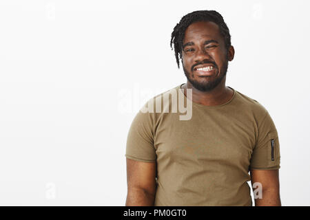 Waist-up shot of positive happy african-american man with beard, winking and smiling broadly with perfect white teeth, feeling joyful while hanging out over gray background with cheerful attitude Stock Photo