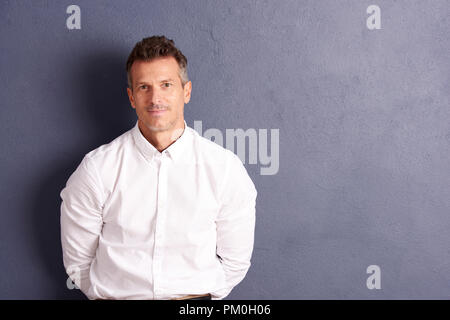 Portrait shot of a middle aged man wearing white shirt and looking at camera while standing at grey wall with copy space. Stock Photo