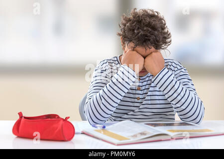 homework. Tired teenager boy doing homework indoors, fists on his eyes Stock Photo