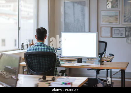 Rearview of a young designer sitting alone at his workstation using a computer while working in an office Stock Photo