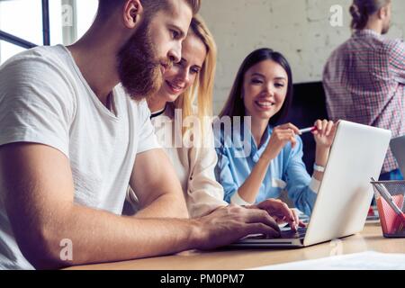 Beautiful business people using gadgets, studying documents, talking and smiling while working in office. Stock Photo