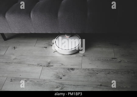 Robotic vacuum cleaner cleaning under the sofa, technological progress, matte effect technique Stock Photo