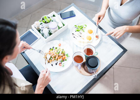 High angle view two unrecognizable women enjoying lunch sitting at table in modern cafe, focus on food Stock Photo