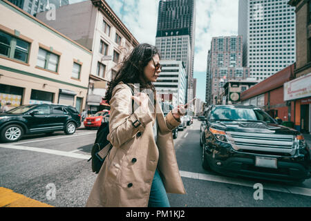 young professional woman crossing the road while using her mobile phone when cars waiting. Stock Photo