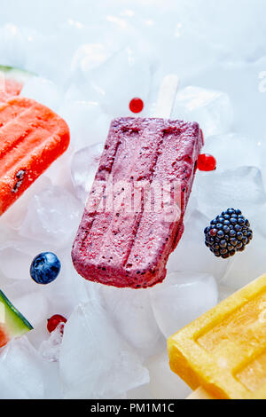 Frozen different fruit juices on a stick on ice cubes with different berries. Sweet healthy dessert. Top view Stock Photo
