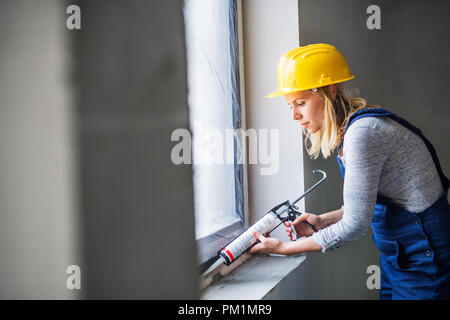 Young woman worker using silicone sealant gun on the construction site. Stock Photo