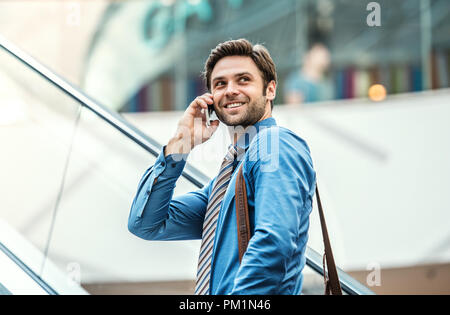 A young businessman going up escalator, talking on the phone. Stock Photo