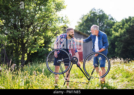 An adult hipster son and senior father repairing bicycle puncture n a sunny day. Stock Photo