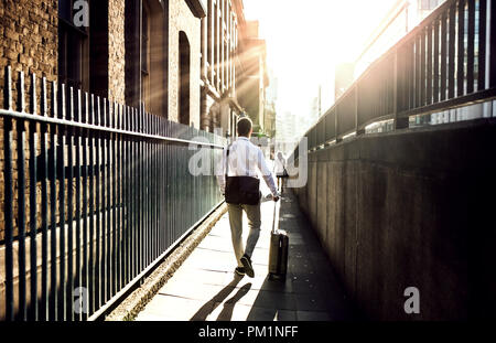 Rear view of businessman with suitcase walking up the street in London. Stock Photo