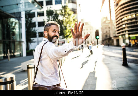 Hipster businessman walking up the street in London, looking back and greeting somebody. Stock Photo
