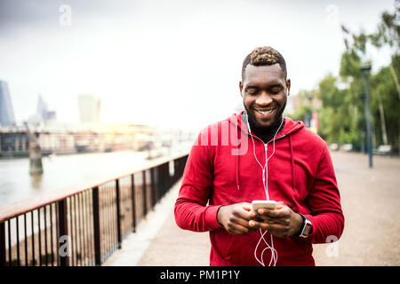 Young sporty black man runner on the bridge outside in a city, using smartphone. Stock Photo