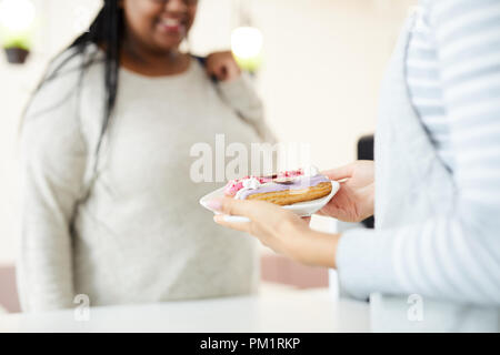 Waiter of cafe or restaurant giving fresh tasty glazed eclairs on plate to one of clients Stock Photo
