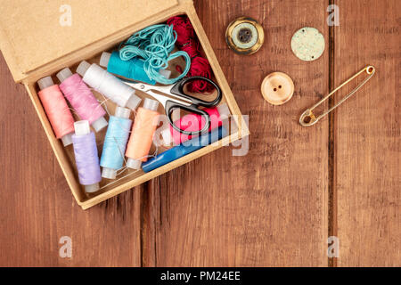 An overhead photo of a sewing box with threads, needles, and scissors, with a vintage pin, buttons, and copy space, shot from above on a dark rustic b Stock Photo