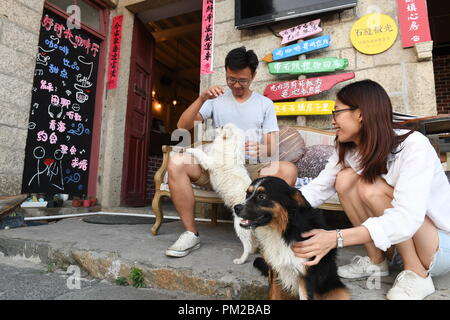 (180917) -- PINGTAN, Sept. 17, 2018 (Xinhua) -- Lin I Chen (R) and her boyfriend Liao Che Wei, both Taiwanese, play with dogs at the 'Rocks Can Sing' art zone in Beigang Village of Pingtan County, southeast China's Fujian Province, Sept. 6, 2018. When tourists get close to 'Rocks Can Sing,' they may see artists playing music with the rocks, and people sipping coffee in rock houses. 'Rocks Can Sing' is an art project which takes in accommodation, live music, restaurant, cafe and souvenir store. Now, a total of 10 young people from the mainland and Taiwan, including Taiwanese Lin I C Stock Photo