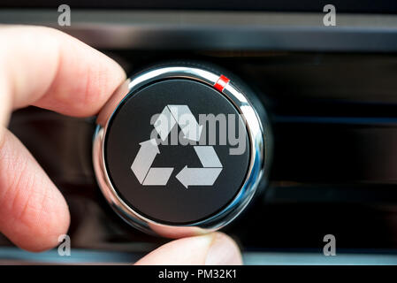 Fingers of a man turning  a button with the recycle icon in white on a piece of electronic equipment. Stock Photo