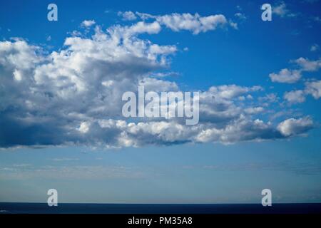 Cloud filled sky, with patches of blue, above a thin sliver of deep blue ocean. Stock Photo