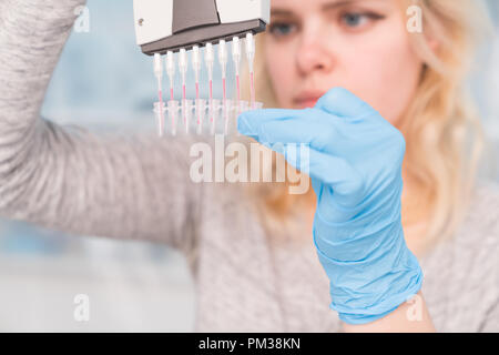 Close up of Young female scientist working in genetics laboratory with pipette in white biological sample Stock Photo