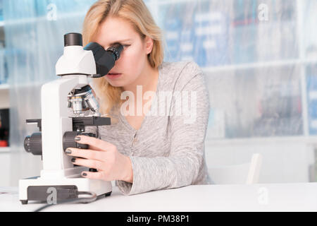 Young woman medical researcher looking through microscop on slide Stock Photo