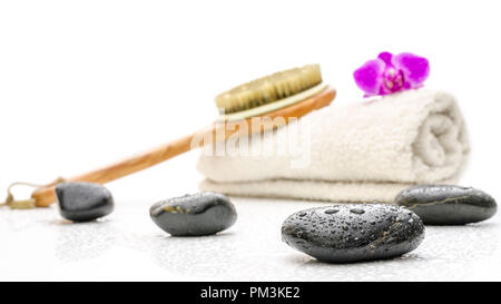 Spa setting with massage stones, brush and a towel. On a white table with water drops. Stock Photo