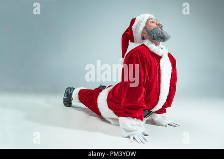 Funny serious guy with christmas hat dancing at studio. New Year Holiday. Christmas, x-mas, winter, gifts concept. Man wearing Santa Claus costume on gray. Copy space. Winter sales. Stock Photo