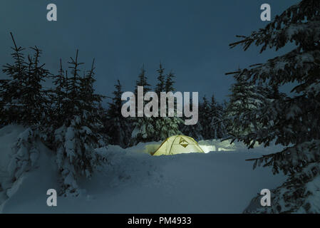 Winter mountain night. Camping in a snowy forest. Night landscape with a tourist tent in a snowbank Stock Photo