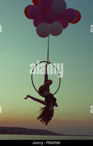 Girl gymnast doing tricks on acrobatic ring at sunset. Stock Photo