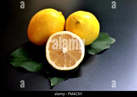 Concept of a group of lemons, two whole and one half on black background. Front view Stock Photo