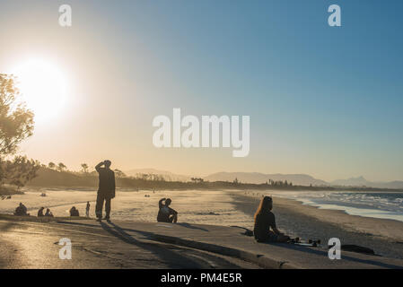 People enjoying the calm and beautiful sunset on the beach, listening the sound of waves and feeling relaxed Stock Photo