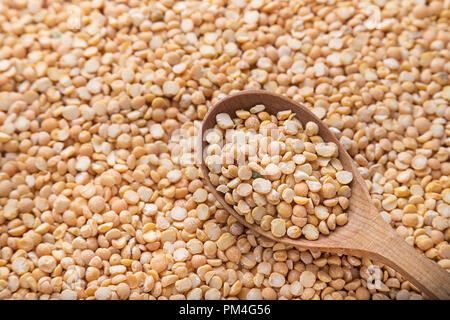 uncooked yellow peas in a wooden spoon on a background of spillage of dry peas Stock Photo