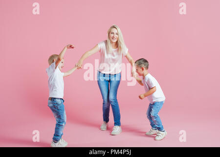 Beautiful blonde mom with two happy sons. Young woman and two baby boys, Jump and dance on pink background Stock Photo