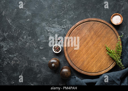 Spices, Herbs, Cutting board for cooking. Round wooden cutting board on black concrete backdrop. Top view with copy space for text. Menu, recipe mock  Stock Photo