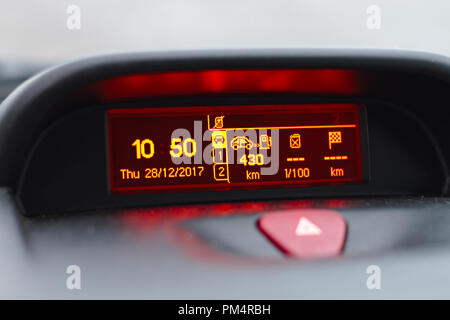 On board computer showing date and time, fuel consumption info and trip length in kilometers. Also hazard warning lights button visible on foreground. Stock Photo