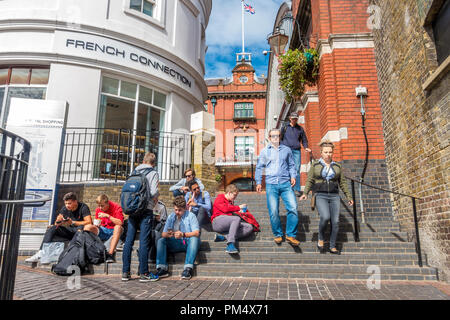 A group of young men sit on steps outside the French Connection store in Windsor, UK. Stock Photo