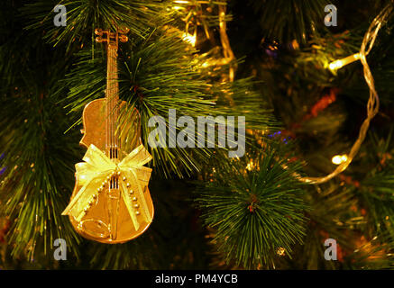 Shiny Gold Cello Shaped with Ribbon Bow Christmas Ornament Hanging on Sparkling Christmas Tree Stock Photo
