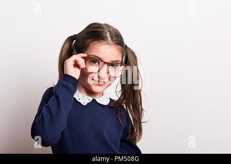 A small cheeky schoolgirl with glasses and uniform in a studio. Stock Photo