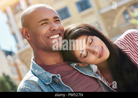 Romantic Relationship. Young diverse couple sitting on the city street hugging girlfriend sleeping on boyfriends shoulder smiling happy close-up Stock Photo