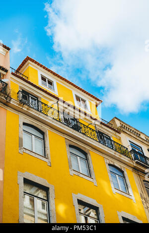 Portuguese architecture of a yellow multi-story building with windows and balconies and a red tile roof; blue sky with clouds. Stock Photo