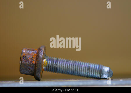 Close photo of an old rusty threaded bolt on the table. Light brown blurred background. Stock Photo