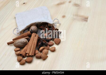 Concept with ingredients for chocolate, cocoa beans, cinnamon, anise, apricot beans coming out of a little bag on natural wood background, side view, Stock Photo