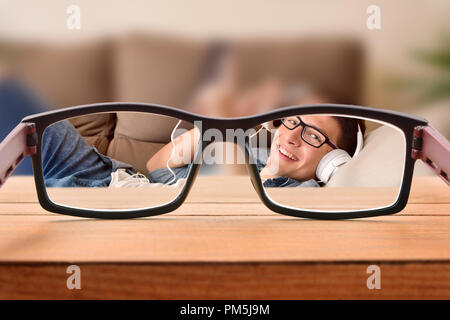 Conceptual view of visual correction with focused scene through eyeglasses of a young man with glasses entertaining lying on a sofa. Stock Photo