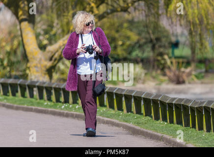 Middle aged woman walking through a park with a camera looking for things to photograph. Stock Photo